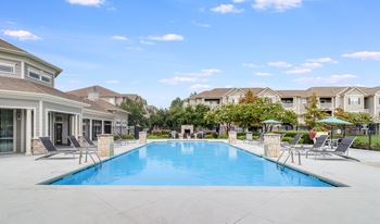 A large swimming pool surrounded by lounge chairs and umbrellas in a residential area.